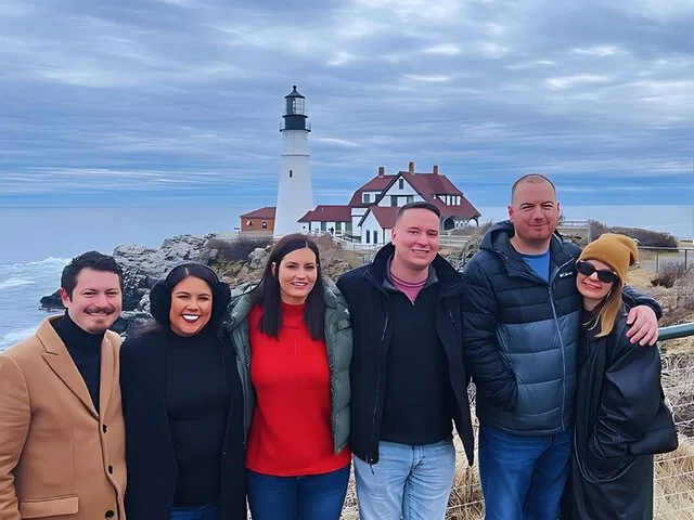 Een groep mensen poseert voor een foto met Portland Head Light op de achtergrond.