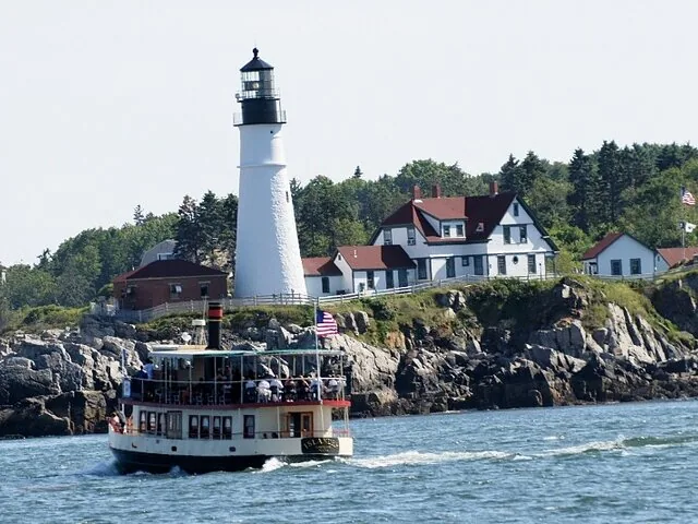 Een kleine rondvaartboot vaart op een zonnige dag langs Portland Head Light.