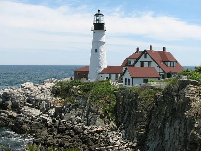 Un faro bianco e la casa del guardiano dal tetto rosso si ergono su una costa rocciosa.