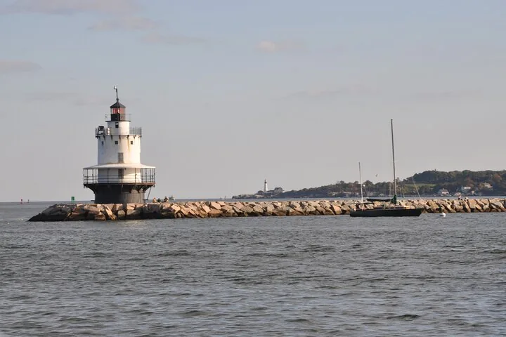 Un faro blanco se erige al final de un largo rompeolas rocoso.