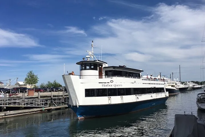 Un gran barco turístico blanco llamado Harbor Queen está atracado en un puerto deportivo.