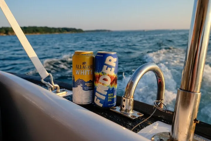 Zwei Bierdosen stehen am Rand eines Bootes, das durch das Wasser fährt.